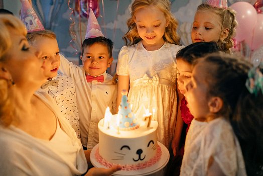 Děti na oslavě narozenin sfoukávají svíčky na dortu ve tvaru kočičky