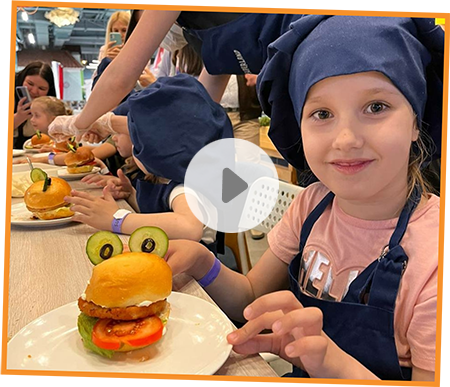 Dívka v kuchařské čepici a zástěře s kreativně ozdobeným hamburgerem ve tvaru žabky