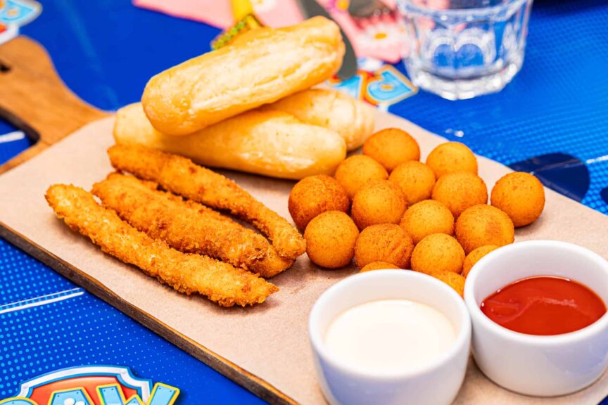 Sýrové tyčinky, bramborové koule, pečivo a omáčky na dřevěném prkénku