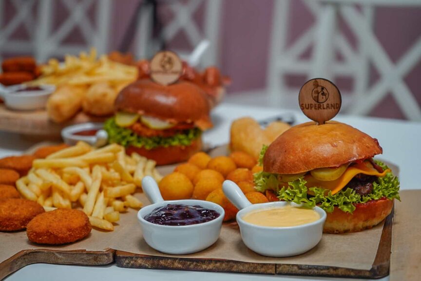 Hamburgery s hranolkami, bramborovými koulemi, nugetami a omáčkami na dřevěném prkénku